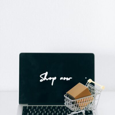 A laptop screen displaying 'Shop now' with a miniature shopping cart and cardboard box.