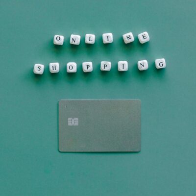 Flat lay of credit card and 'Online Shopping' text on green background, symbolizing ecommerce.