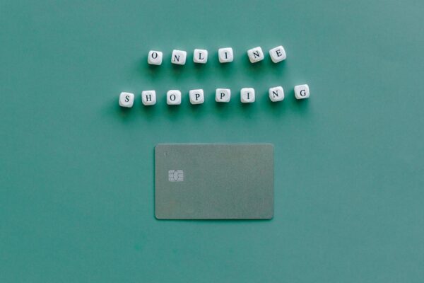 Flat lay of credit card and 'Online Shopping' text on green background, symbolizing ecommerce.